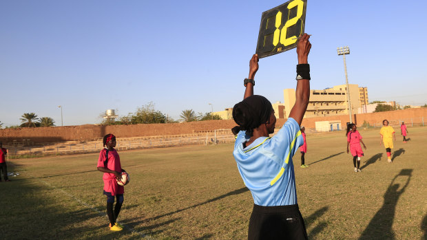 A referee holds a board as Sudanese al-Difaa, in pink, and al-Sumood women's teams play in Omdurman.