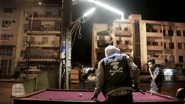 Young people play pool on a street in front of damaged buildings in Aden.