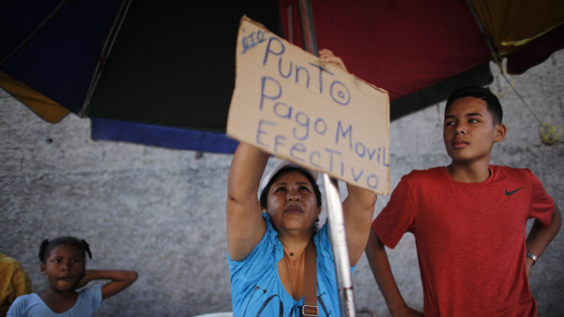 Daixy Aguero puts up a sign that reads in Spanish "Point of sale, mobile payment and cash," at her stand where she sells beauty products, at a market in Caracas, Venezuela. 