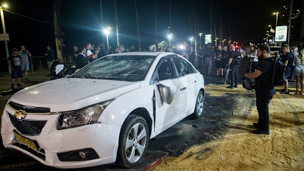 An Israeli police officer inspects the damaged car of an Israeli Arab man who was attacked and injured by an Israeli Jewish mob in Bat Yam, Israel.