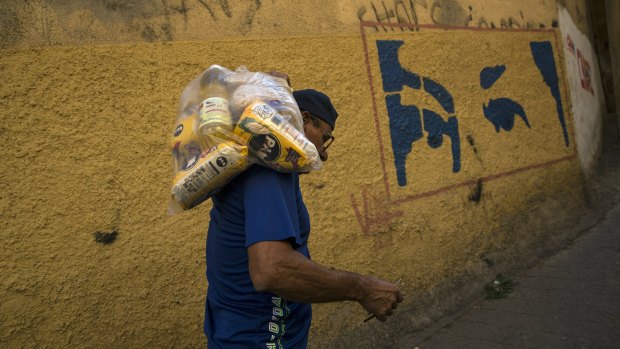 With a mural depicting the eyes of Veneuzela's late President Hugo Chavez, Carlos Gonzales carries a bag with food delivered by the government for the poorest people in the Antimano neighbourhood of Caracas, Venezuela.