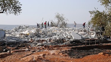 People look at a destroyed houses near the village of Barisha, in Idlib province, Syria.
