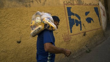 With a mural depicting the eyes of Veneuzela's late President Hugo Chavez, Carlos Gonzales carries a bag with food delivered by the government for the poorest people in the Antimano neighbourhood of Caracas, Venezuela.