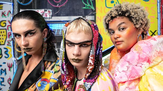 Models Eloise Humphrys, Elliot Cowen and Milo Hartill  ahead of the Romance Was Born ‘Stronger Together’ show with artist Paul Yore’s installation ‘Word Made Flesh’ at Carriageworks as a backdrop on February 21, 2023, in Sydney. 