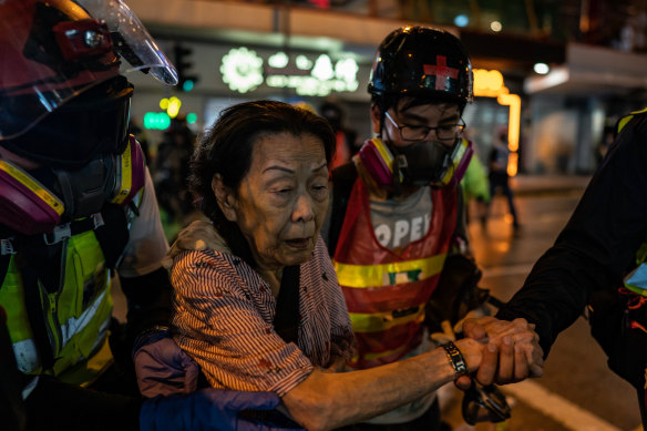 Volunteer medics help a woman cross a road during a clash between police and protesters in Causeway Bay district in August.