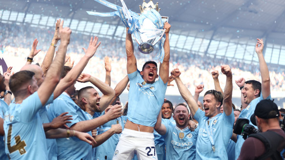 Matheus Nunes holds the Premier League trophy aloft as Manchester City celebrate their title victory.