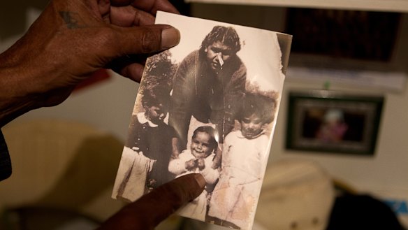Kutcha Edwards holds a photo of himself as a child with his sisters, Maria and Alice, and cousin Mary Briggs, nee Edwards.