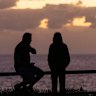 People gather by a coffee truck on the southern headland at Avalon Beach to watch the sunrise.