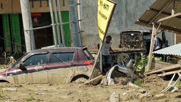 Two desperate locals searching  trapped and damaged cars to siphon the fuel off in Palu.