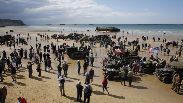 People walk among vintage World War II vehicles parked on the beach during events to mark the 75th anniversary of D-Day in Arromanches, Normandy, France.