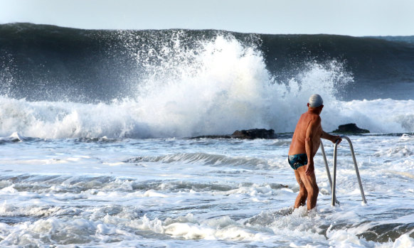 An ocean swimmer watches on as a wave rears up at Austinmer Beach on Saturday morning.