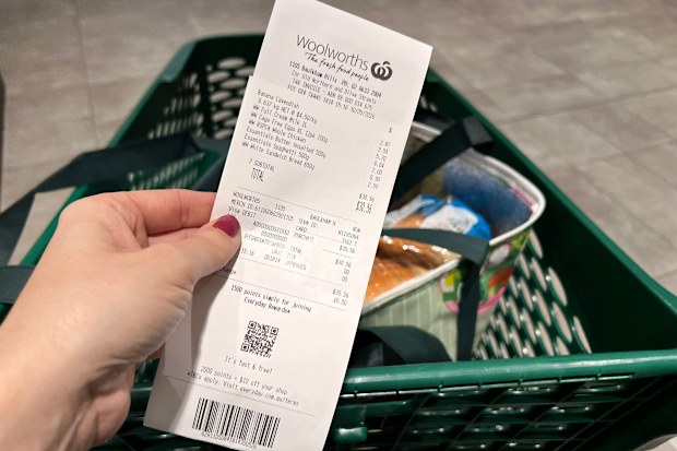 A Woolworths receipt being held up in front of a Woolworths trolley.