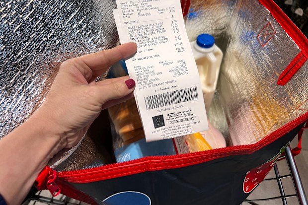 A Coles receipt being held up in front of a trolley containing a bag of groceries.