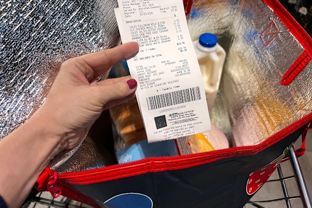 A Coles receipt being held up in front of a trolley containing a bag of groceries.