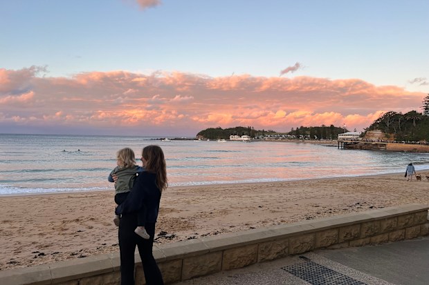 Woman and toddler standing by the beach at sunset