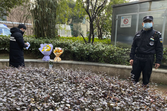 A security guard stands neaby as a man visiting the Wuhan Central Hospital leaves flowers in memory of whistleblower doctor Li Wenliang.