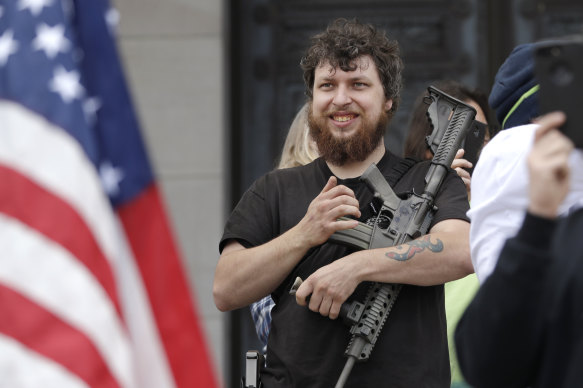 Kevin King cradles an assault rifle as he stands on the top of the Capitol steps at a protest opposing Washington state's stay-home order to slow the coronavirus outbreak on Sunday, in Olympia.