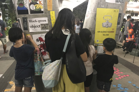 A family write messages on Lennon Wall on a pedestrian bridge above Harcourt Road, before police clear the road with a water cannon.
