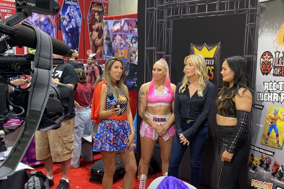 Wrestler Kandi Krush (Amberley Shaw), LA Lakers owner/president and WOW co-owner Jeanie Buss, and wrestler Genesis (Selena O’Sullivan) speak to reporter Ariana Cohen (far left) at Comic-Con.