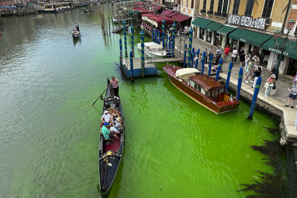 A gondola crosses Venice’s historical Grand Canal as a patch of phosphorescent green liquid spreads.