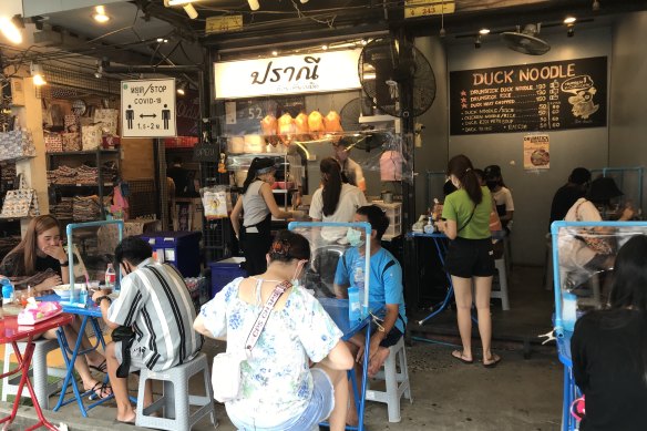 At an eatery at the Chatuchak Weekend Market in Bangkok, partitioned tables and social distancing signs separate a few local customers. Foreigners, the market's main visitors, are still not allowed in the country.