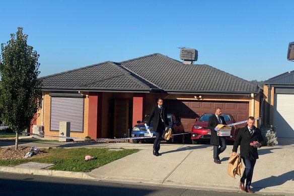 Detectives carrying items in brown paper bags from the house.