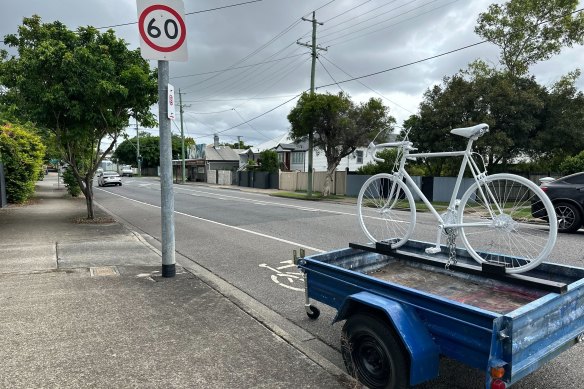 The ghost bike memorial on Nudgee Road at Hendra has reappeared on the back of a legally parked trailer. There is a “No Standing” sign pointing the other way, and a bicycle stencil on the road, but the trailer is in a legal parking space.