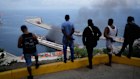 Men watch smoke rising from a dock after Venezuela’s La Guaira port was targeted by US forces.
