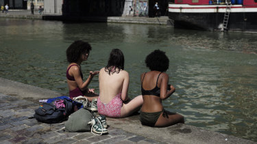 Girls wearing swimsuits sit along the Canal de l'Ourcq in Paris.