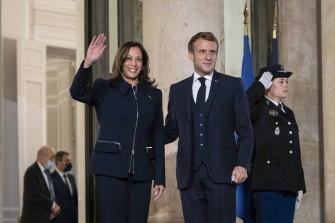 French President Emmanuel Macron stands next to US Vice President Kamala Harris as she waves before a bilateral meeting.