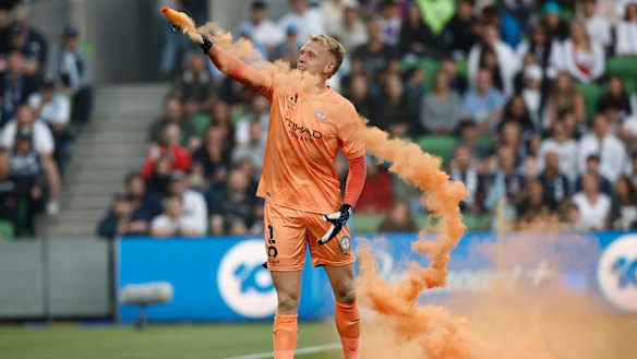 Melbourne City goalkeeper Tom Glover picks up a flare to remove it from the field.