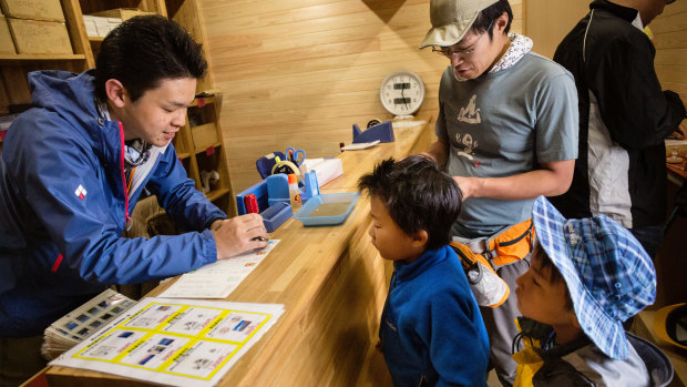A hiker and his sons arrange to have postcards sent from the post office on the summit of Mount Fuji.