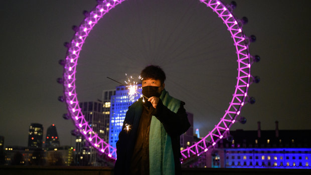 A man holds a sparkler in front of the London Eye, in what would normally be a ticket-only area filled to capacity waiting for the annual fireworks display in London, United Kingdom. 