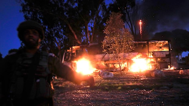 An Israeli soldier stands near a burning bus after it was hit by a mortar shell fired from Gaza on Monday. 