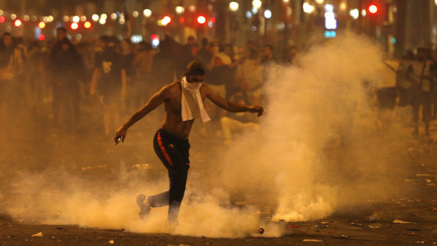 A man kicks a tear gas canister thrown by riot police during clashes on the Champs Champs Elysees avenue where soccer fans were celebrating France's World Cup victory.