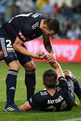 Distraught: Antonis is helped to his feet by captain Carl Valeri after scoring an own goal against Sydney FC.