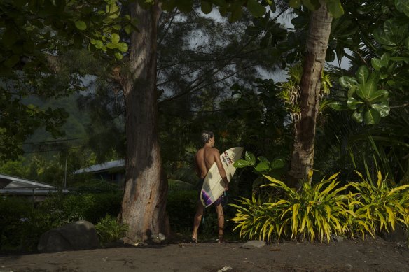 A surfer walks along the beach in Teahupoo.