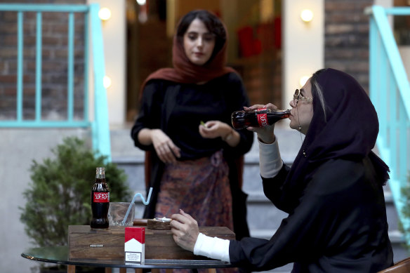 An Iranian drinks a Coca-Cola and smokes a Marlboro cigarette at a cafe in downtown Tehran.
