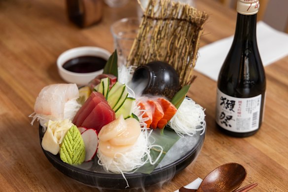Tuna, kingfish, and salmon sashimi arrive wreathed in dry-ice fog against a sculpted backdrop of cucumber and radish.