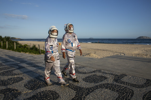 Tercio and Alicea Galdino, dressed in protective astronaut costumes, walk along Ipanema beach in Rio de Janeiro.