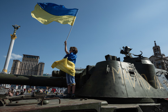 A boy holds a Ukrainian national flag on a captured Russian tank in central Kyiv.