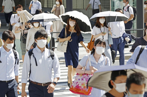 Commuters use parasols to shield themselves from the sun in Tokyo on Monday.