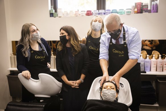 Prime Minister Scott Morrison washes the hair of an employee of Cocos Hair Salon in Mount Eliza on Friday.