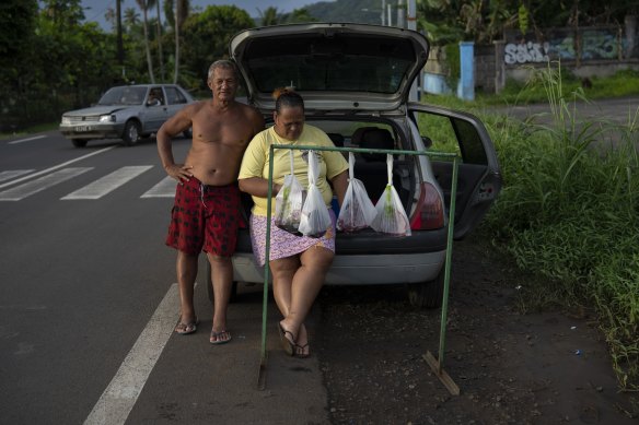 A couple sells bags of fresh tuna on the side of the road in Teahupoo.