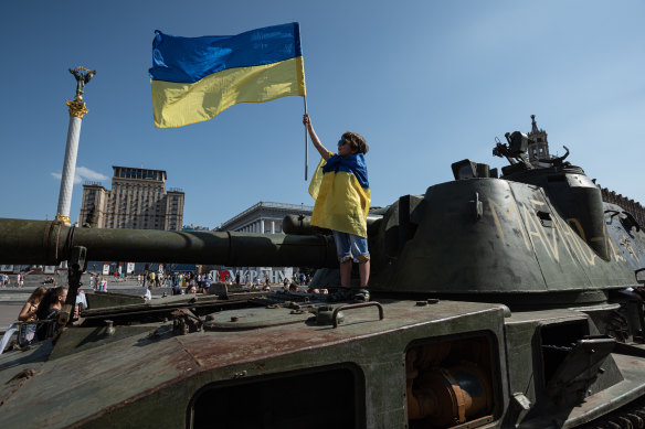 एक लड़का स्वतंत्रता दिवस से पहले कीव में प्रदर्शन के लिए एक रूसी टैंक पर यूक्रेनी झंडा रखता है।