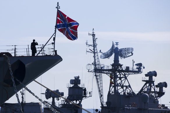 A Russian sailor salutes on the bow of missile cruiser Moskva, left, as crew of Russian patrol ship Pitliviy, right, prepare to moor the vessel, in Sevastopol, Crimea. 