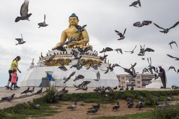 Pigeons fly past a Buddha statue in Darkhan, Mongolia.