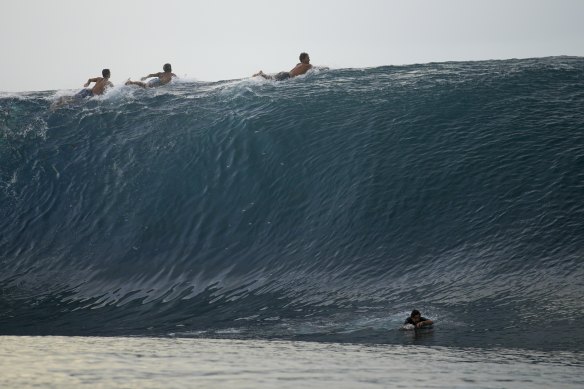 Surfers paddle over the crest of a wave in Teahupoo, Tahiti.