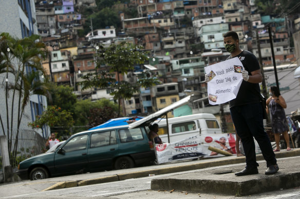 Felipe Feliz, resident of Morro do Borel community, holds a sign that reads in Portuguese 'Can you donate 1kg of food?' during the pandemic in Rio de Janeiro.