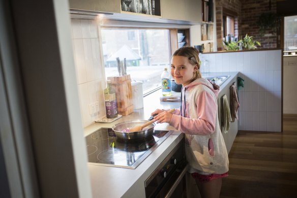 Josie Aberle cooks a meal on an induction cooker. Her parents chose not to connect their house to gas, and also installed a reverse cycle air-conditioner and heat pump hot water. 